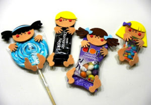 Quatro figuras de crianças feitas com recortes de EVA, cada uma segurando diferentes doces, como pirulito, chocolate, amendoim confeitado e balas coloridas, sobre uma superfície branca.