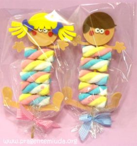 Lembrancinha feita com marshmallows coloridos em formato de menino e menina, embalados em celofane e decorados com laços, ideal para festas infantis.
