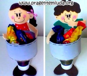 Dois potes reciclados decorados com personagens de menino e menina feitos em EVA, utilizados como lembrancinhas escolares com doces coloridos dentro.